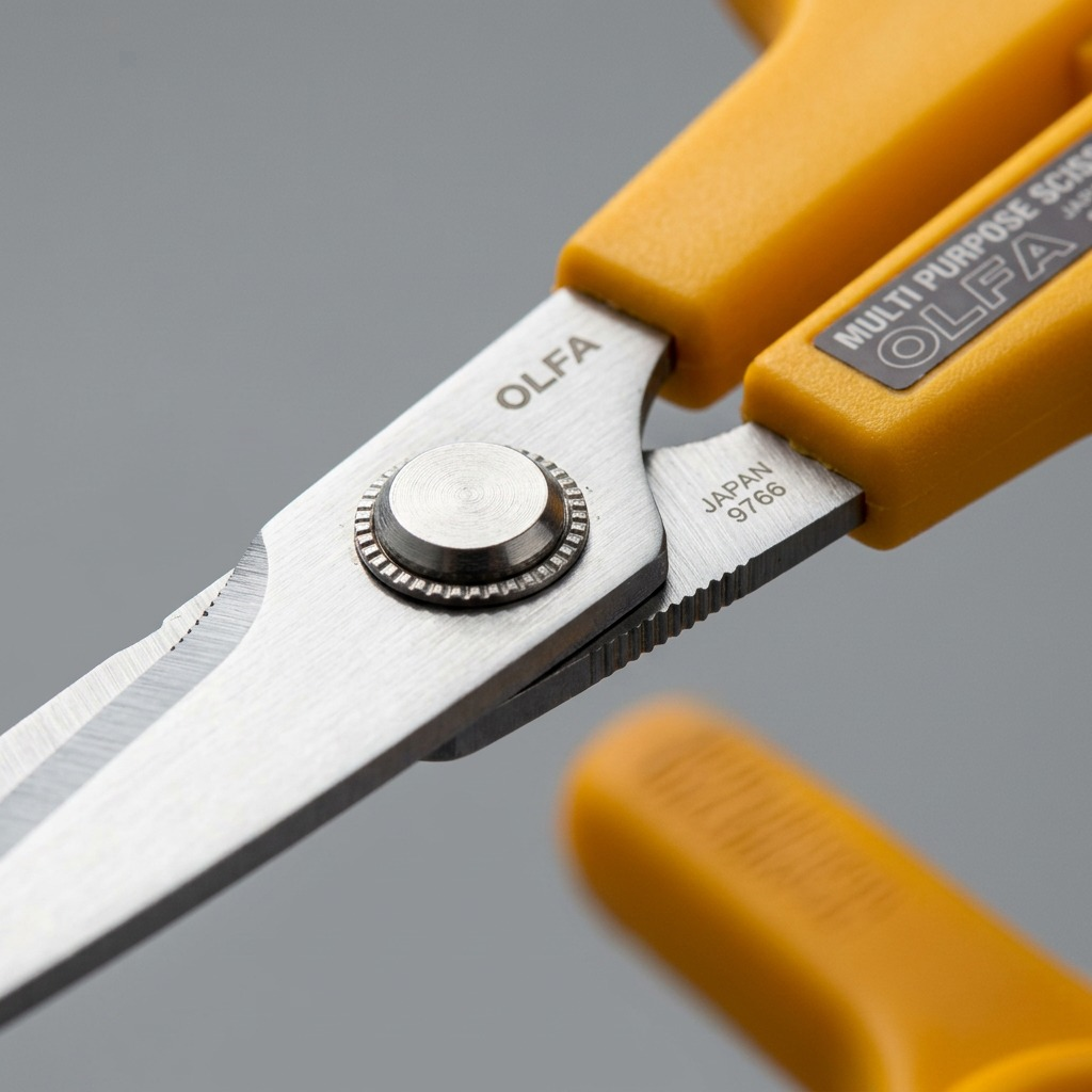 Macro close-up of Olfa SCS-2 scissors, focusing on the rivet hinge and serrated blade texture.