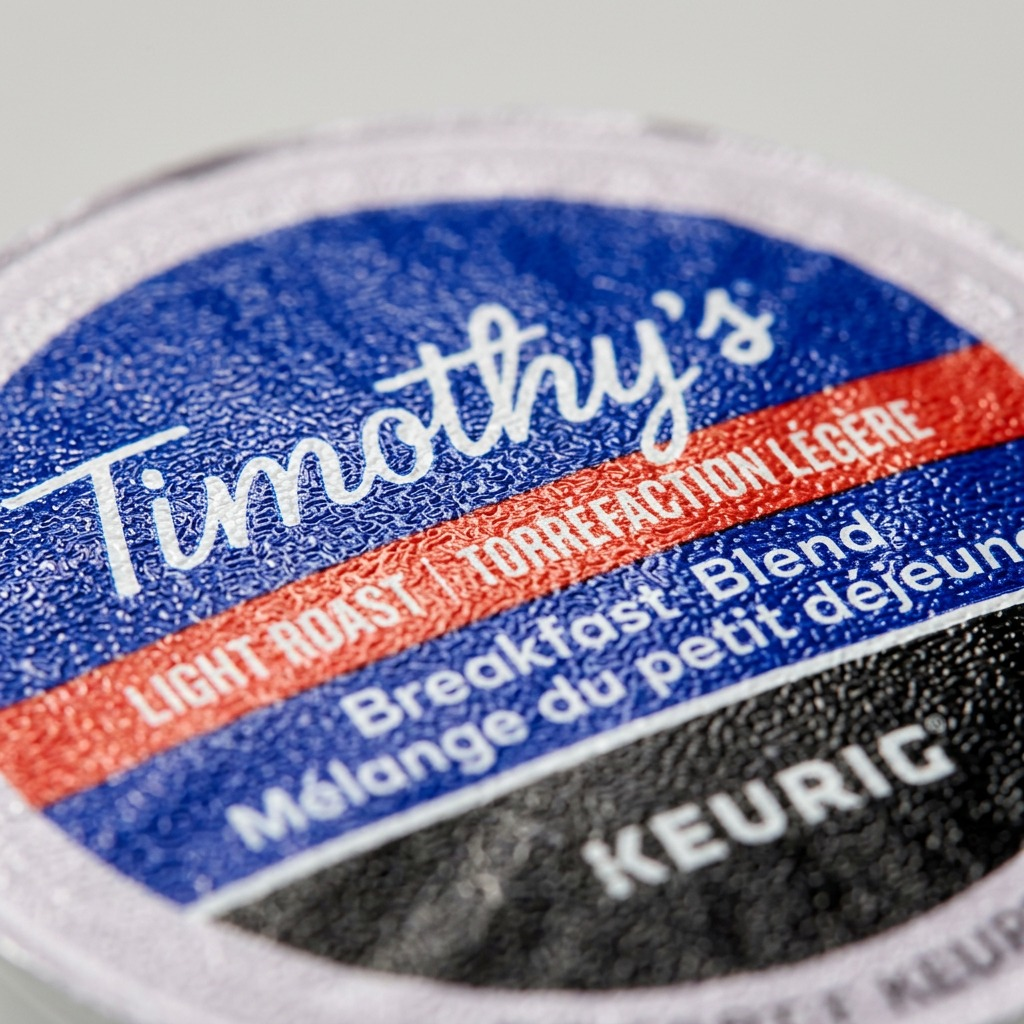 Mentally-precise macro close-up of a Timothy's Breakfast Blend K-Cup pod. The central "Timothy's" script, light roast level, and "Keurig" logo show sharp, high-quality printing on a tactile plastic lid.