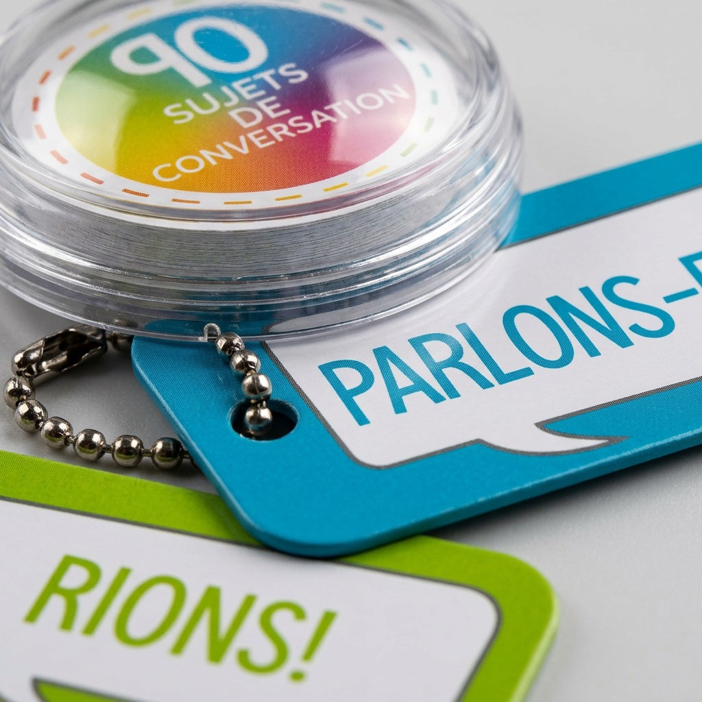 A close-up photograph of three colorful circular tags on a metal ball chain, with a clear blue tag in the center.