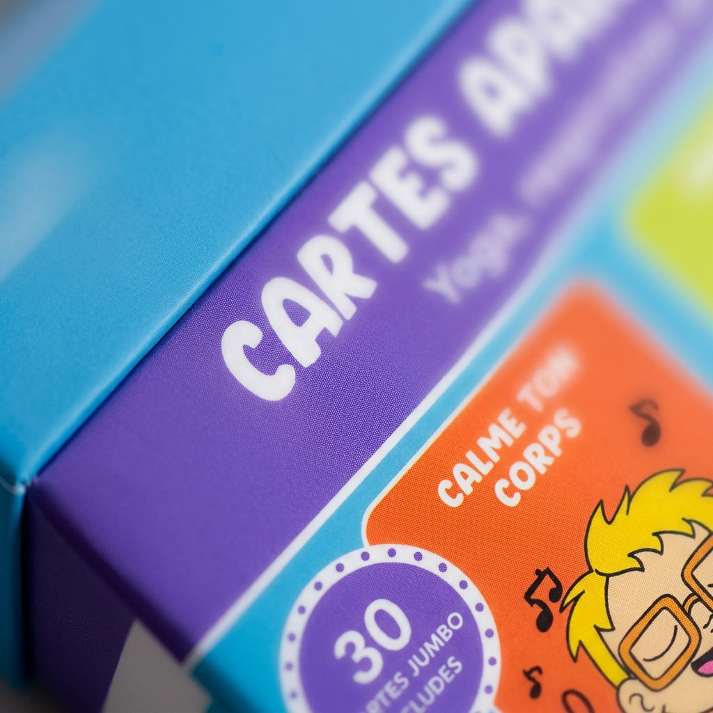 A macro-photographic close-up of the fdmt Cartes apaisantes jumbo box, showing the texture of the laminated chipboard lid over the purple body. The focus is sharp on the purple printed area featuring "CARTES APAISANTES JUMBO", and adjacent sections.